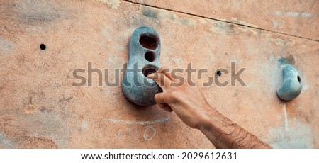 Close-up photo of male hand gripping climbing holds on worn wall outside. Man doing bouldering exercise on artificial rock climbing parkour at park.