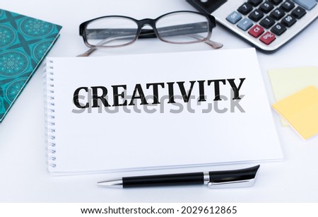 notebook with text Creativity on a white background next to glasses, a pen
