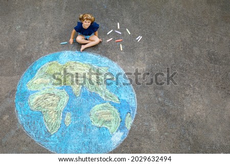 Little preschool girl with earth globe painting with colorful chalks on ground. Positive toddler child. Happy earth day concept. Creation of children for saving world, environment and ecology. Royalty-Free Stock Photo #2029632494