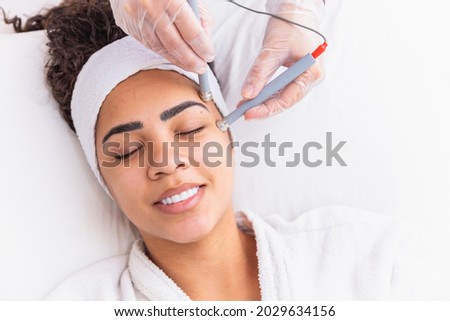 Young woman lying on cosmetologist's table during rejuvenation procedure. Cosmetologist take care about neck and face skin youthfull and wellness. Hardware face cleaning procedure.