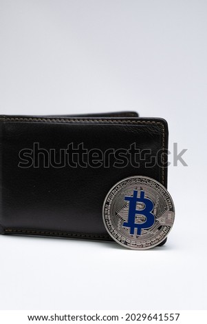 Silver Bitcoin coin with Logo in Blue in front of half opened brown leather wallet sitting on light grey background. Bitcoin BTC Digital crypto currency - Electronic Money. Digital coin international.