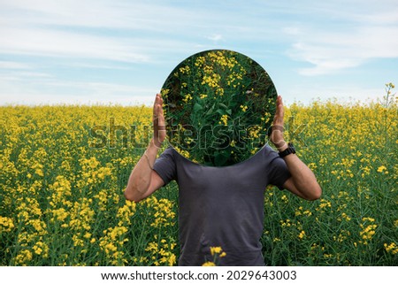 Man standing in yellow flowers field and holding circle mirror. Creative travel concept