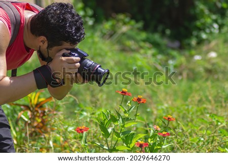 A closeup of a Hispanic man taking pictures of vibrant flowers while wearing a Covid mask