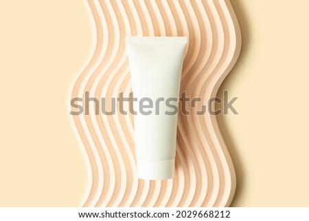Blank white cosmetics tube on the beige background.Wavy podium under it.Good as cosmetic mockup,pastel banner with copy space.