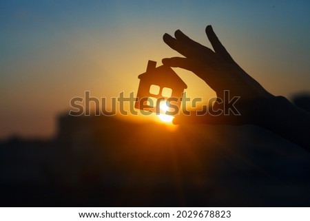 Man holding  wooden house model against sunset light for sale or rent, family home and shelter concept, real estate, solar energy and eco accommodation