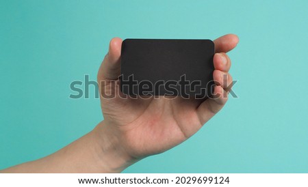 Male hand holding black blank card isolated on mint green or Tiffany Blue background.