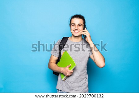 Happy young man with backpack walking and talking on mobile phone over blue background