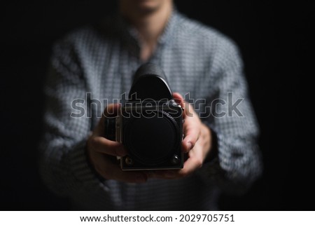 man on black background holding old medium format film camera