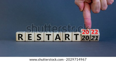 2022 restart new year symbol. Businessman turns a wooden cube and changes words 'Restart 2021' to 'Restart 2022'. Beautiful grey background, copy space. Business, 2022 restart new year concept.