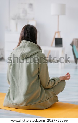 meditation and yoga at home, beautiful and young European woman doing yoga and breathing practices in her home. woman sitting in lotus pose with eyes closed, green suit for sports, beautiful cozy