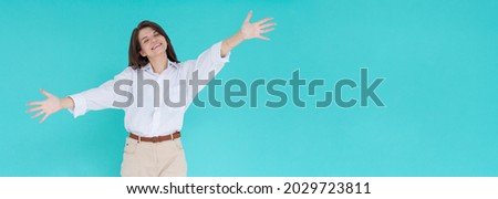 Smiling young brunette woman girl in white shirt posing isolated on pastel blue wall background studio portrait. People lifestyle concept. Mock up copy space. Standing with outstretched hands
