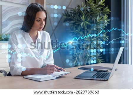 Attractive businesswoman in white shirt at workplace working with laptop to optimize trading strategy at corporate finance fund. Forex chart hologram over office background