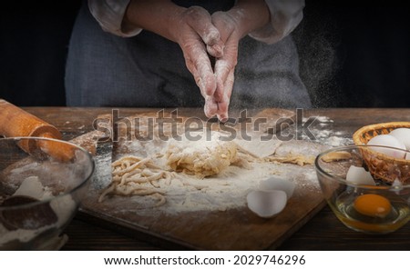 Women's hands, flour and dough. A woman, in an apron cooking dough for homemade baking, a rustic home cozy atmosphere, a dark background with unusual lighting.