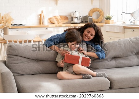 Birthday gift for small kid: joyful caring mom greeting child presenting little preschool boy present box for holiday event. Happy son enjoy mother care and love. Parenthood and celebration concept