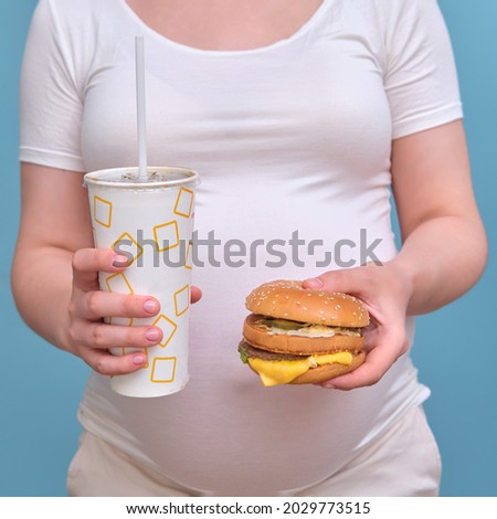 Pregnant woman with a hamburger and soda on a blue background, close-up