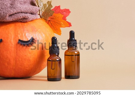 mock up set of cosmetic containers with pipettes from amber glass and pumpkin with towel and false eyelashes on beige background, natural skin care in autumn concept