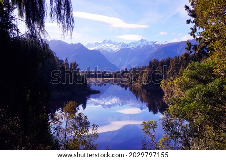 Lake Matheson with a reflection. Mountain Mt Cook and Mt Tasman with snow and glaciers on the top in the background. Some clouds and unfortunately a little bit windy. Nice beautiful morning in autumn 