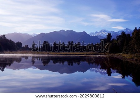 Beautiful morning in Lake Matheson, West Coast, New Zealand. Perfect reflection is unreal. Some mist above water. Trees like silhouettes around the lake. Mt. Cook and Mt Tasman are in the background. 