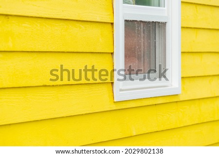 The exterior of a bright yellow narrow wooden horizontal clapboard wall of a vintage house. The wooden trim on the building is white in color. The outside boards are textured pine wood.