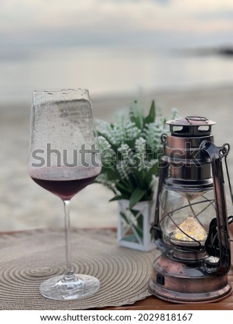 Red wine in a wine glass on a wooden table by the sea, decorated with lanterns and flowers.