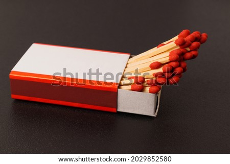 Matches in an open matchbox on a black background. A blank, white label on the matchbox.