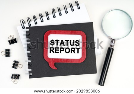 Business concept. There is a magnifying glass, a notebook and a sign on the table - STATUS REPORT