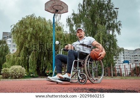 A man in a wheelchair plays basketball on the sports ground. The concept of a disabled person, a fulfilling life, a person with a disability, fitness, activity, cheerfulness.