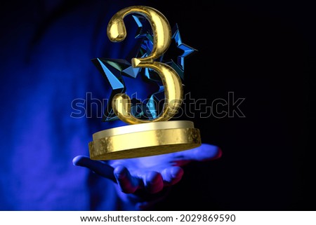 A male's hand holding a 3D rendering of a 3rd place award on a blue background