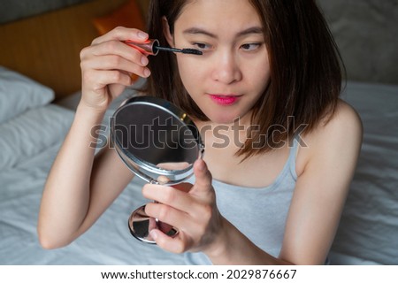 Portrait of young Asian woman applying black mascara on her eyelashes with a wand applicator. Mascara is a cosmetic commonly used to enhance the eyelashes.