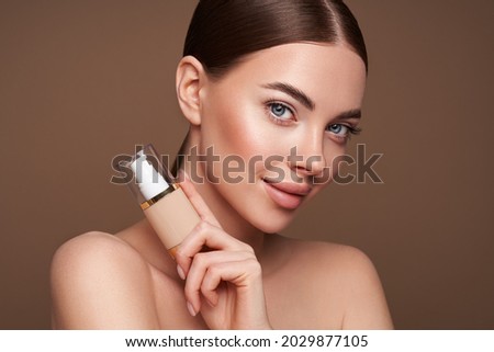 Portrait beautiful young woman with clean fresh skin. Model with foundation makeup bottle. Cosmetology, beauty and spa Royalty-Free Stock Photo #2029877105