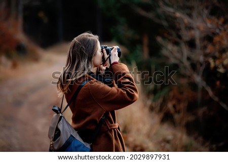 Woman with camera makes a photo in mountain forest 