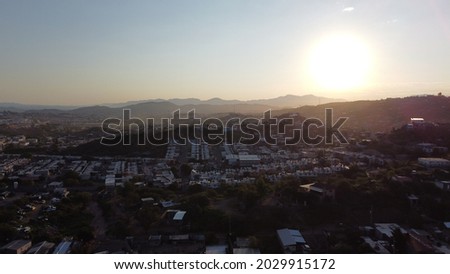 An aerial view of cityscape with dense buildings and hills under a clear sky at sunset