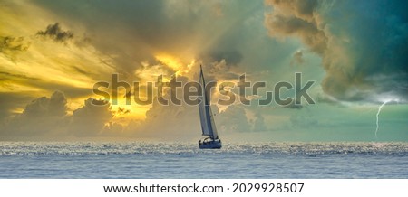 Sailboat navigating a silvery sea in a stormy cloudy sunset