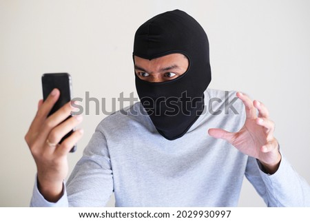 A bad guy wearing balaclava trying to steal someone personal data using mobile phone
