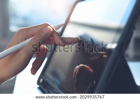 Close up of business woman hand with stylus pen using digital tablet, finger touching on screen on office table. Female graphic designer working on mobile app via digital tablet, technology concept