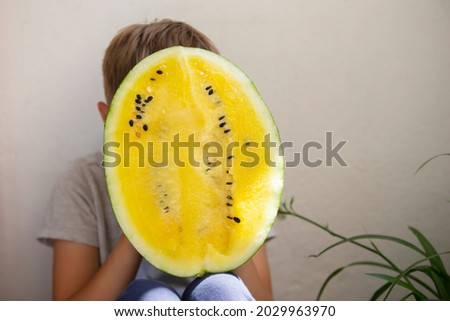 The boy covered his face with a large yellow watermelon.