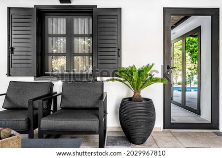 Outdoor terrace. Dark grey color armchairs, flower pot and window shutters with the white wall at the background. Selective focus. Royalty-Free Stock Photo #2029967810