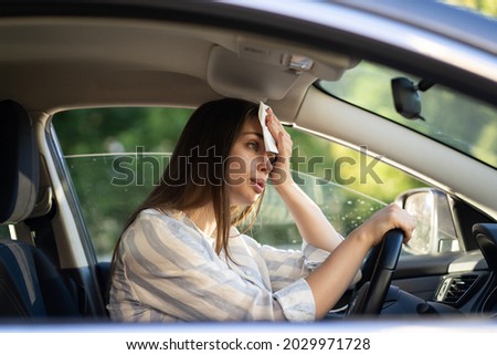 Girl driver being hot during heat wave in car, suffering from hot weather, has problem with a non-working air conditioner, wipes sweat from her face with tissue. Summer, heat concept.  Royalty-Free Stock Photo #2029971728