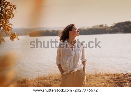 Beautiful young relaxed woman in white blouse enjoying nature breathing fresh air meditating on the river on an autumn Royalty-Free Stock Photo #2029976672