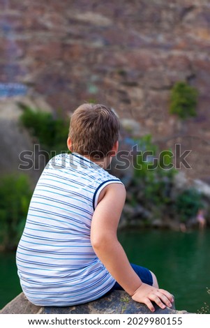 A child sits on the top of a beautiful canyon and looks at the water in it. The bank of the canyon. Portrait of a child.