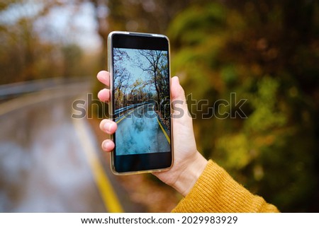A female hand holding an mobile Phone trying to capture the awesome colors of autumn in the forest. Fall Getaway