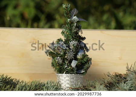 A small artificial Christmas tree in Christmas balls on the background of a wooden board on a clear winter day.