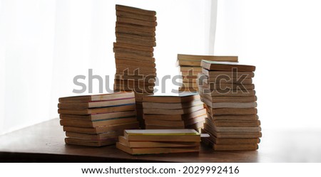Old manga books stacked up by the window on a old wooden desk.