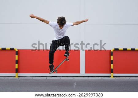 young skater does tricks outdoor. background is white and red wall Royalty-Free Stock Photo #2029997060