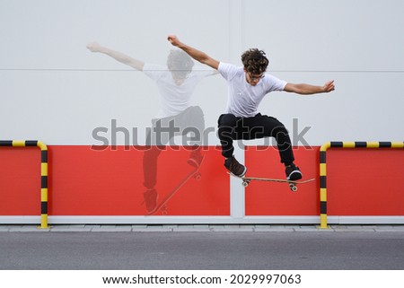 young skater does tricks outdoor. background is white and red wall