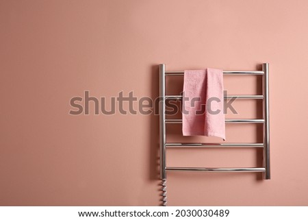 Modern heated towel rail with warm soft towel on light pink wall. Space for text