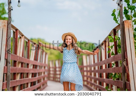 A happy little girl in a blue dress in a summer garden with a wooden bridge. Concepts of summer holidays and a fun childhood