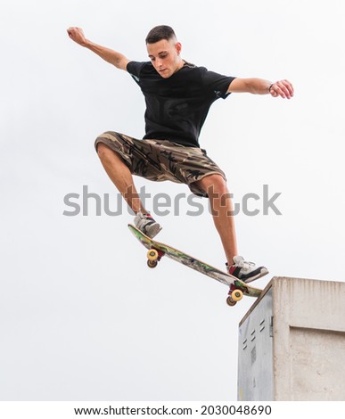 Young skateboarder in shorts jumping a wall in an urban environment. Royalty-Free Stock Photo #2030048690