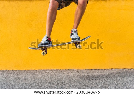 View of man on shorts legs jumping with skateboard on yellow background. Royalty-Free Stock Photo #2030048696