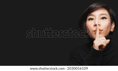 Beauty secret concept - Close up head shot face of an asian stylish woman in black looking to camera and doing Shh hand sign gesture to her lips. Surprised, Background, Copy space, Studio portrait.